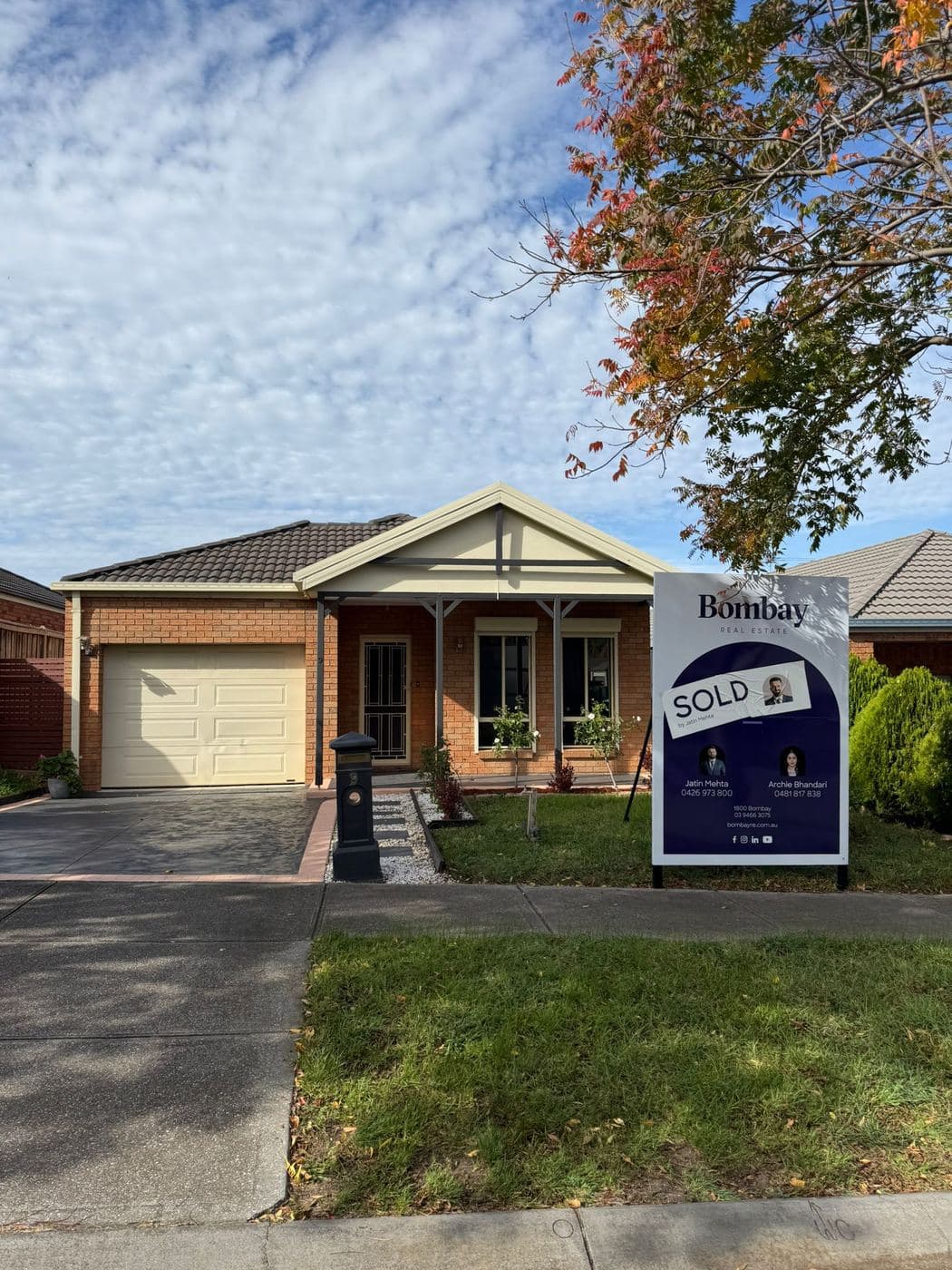 A sold board outside a brick home under an autumn tree