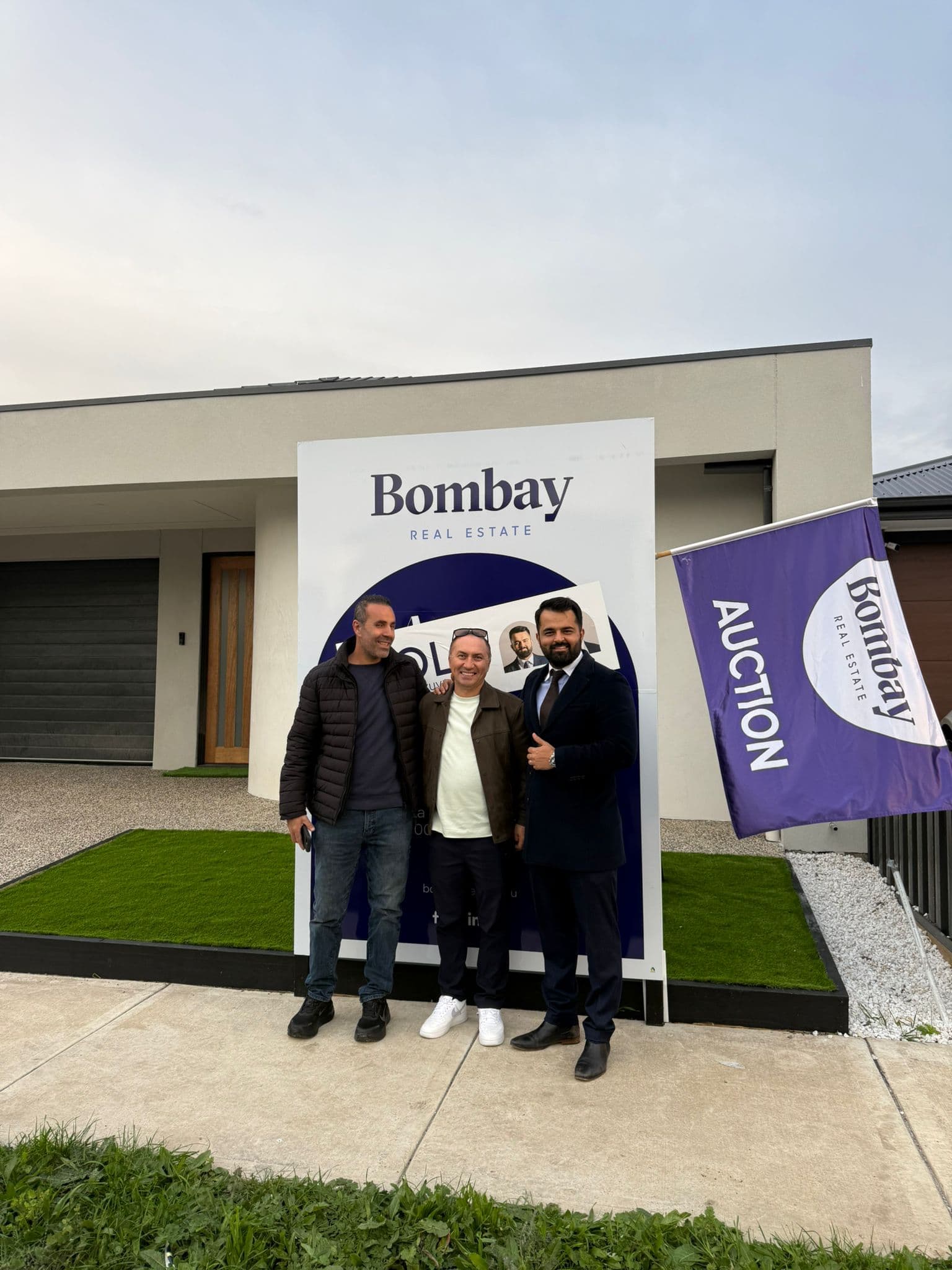 Buyers with their agent at a sold board and auction flag